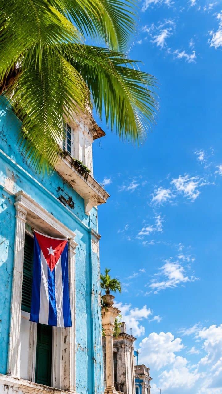 Fachada azul de La Habana con una bandera cubana en el balcón y palmeras