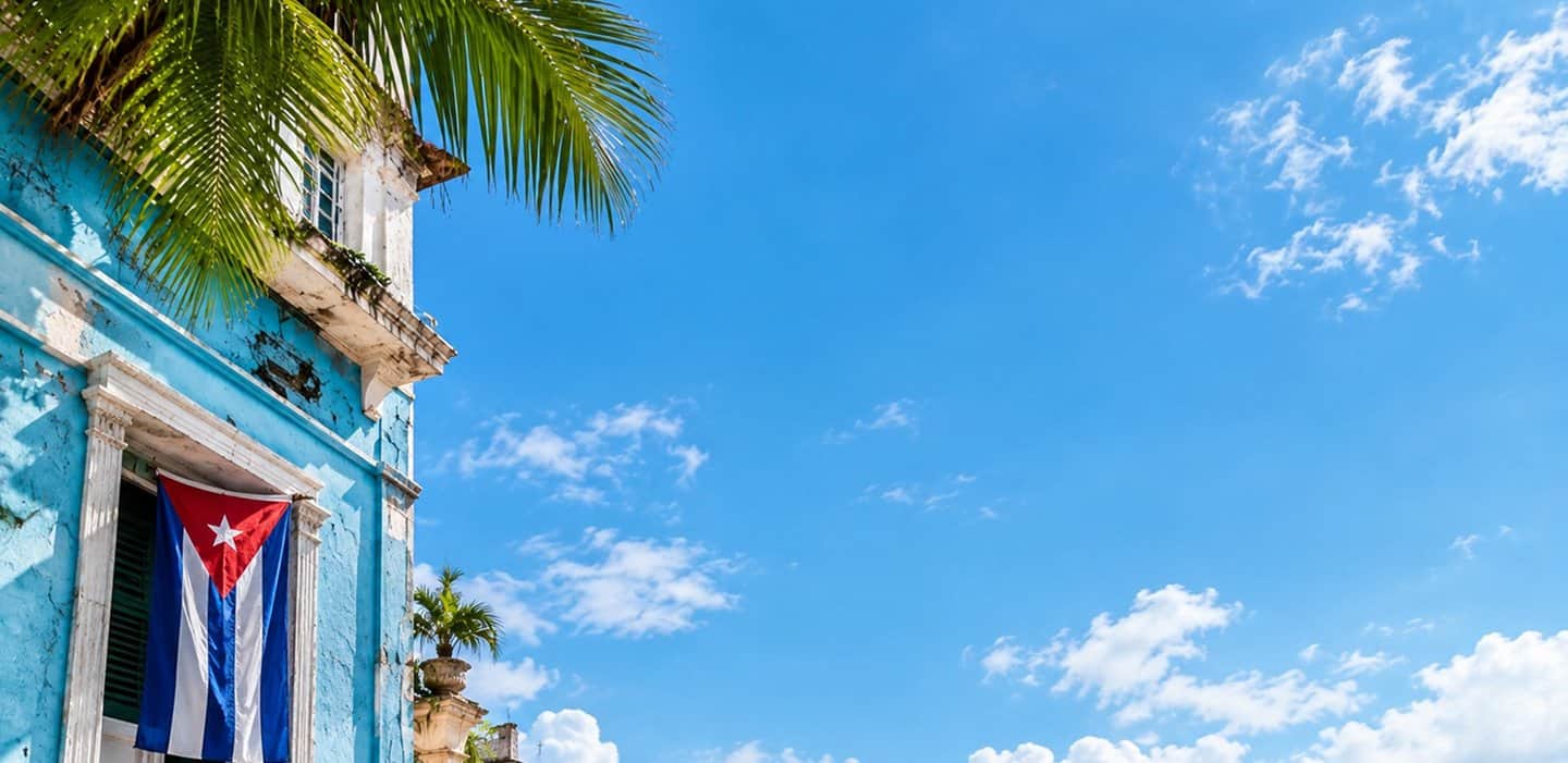Fachada azul de La Habana con una bandera cubana en el balcón y palmeras